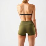 Back view of a woman wearing olive green yoga shorts, showcasing fit and cut on white studio background.