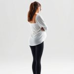 Back view of a model wearing black maternity pants pregnancy leggings in white, showcasing fit on pure white studio background.