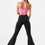 Back view of a model wearing flare black yoga pants with a pink gym top, showcasing fit on white background.