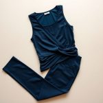 Navy blue wrap tie top and yoga pants folded flat on a neutral surface.