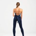 Back view of a model wearing a navy blue wrap tie top and yoga pants on a white background.