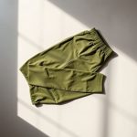 Olive Green yoga pants men neatly folded, male yoga attire in minimalist flat lay on neutral surface.