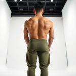 Back view of a man wearing olive green yoga pants men male yoga attire, studio shot on white background.